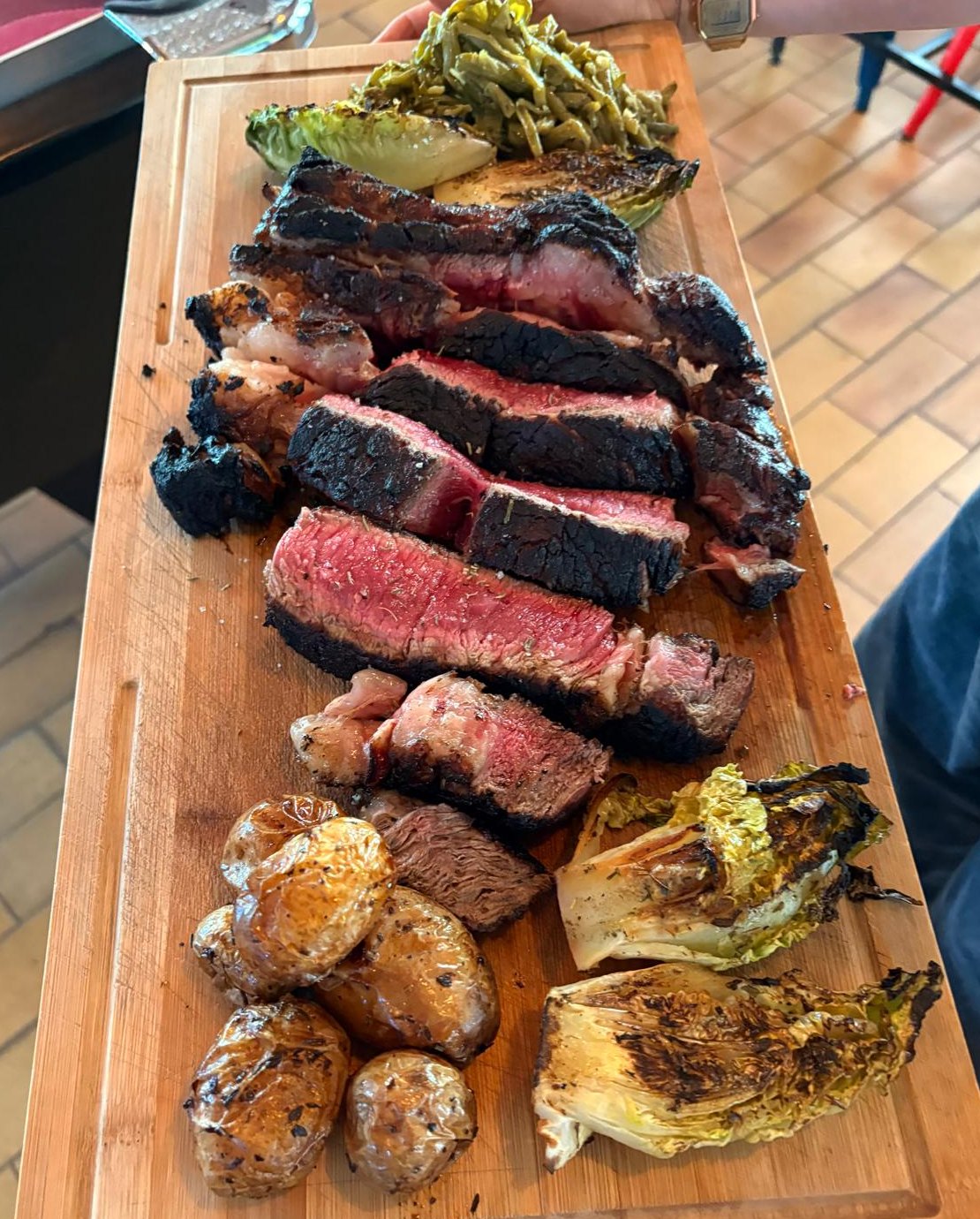 La côte de bœuf tranchée sur planche, avec pommes de terre grillées et sucrines à la braise